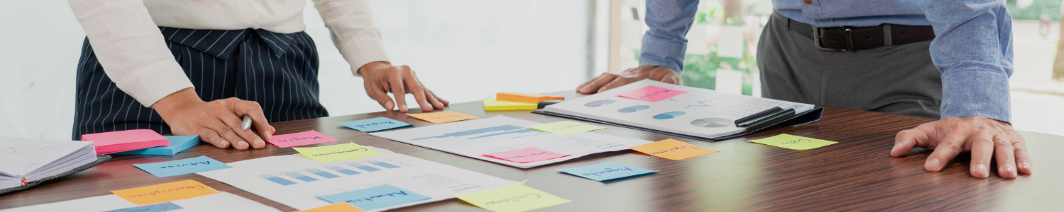 Zwei Personen stehen vor einem Tisch mit Papieren und bunten Post-Its